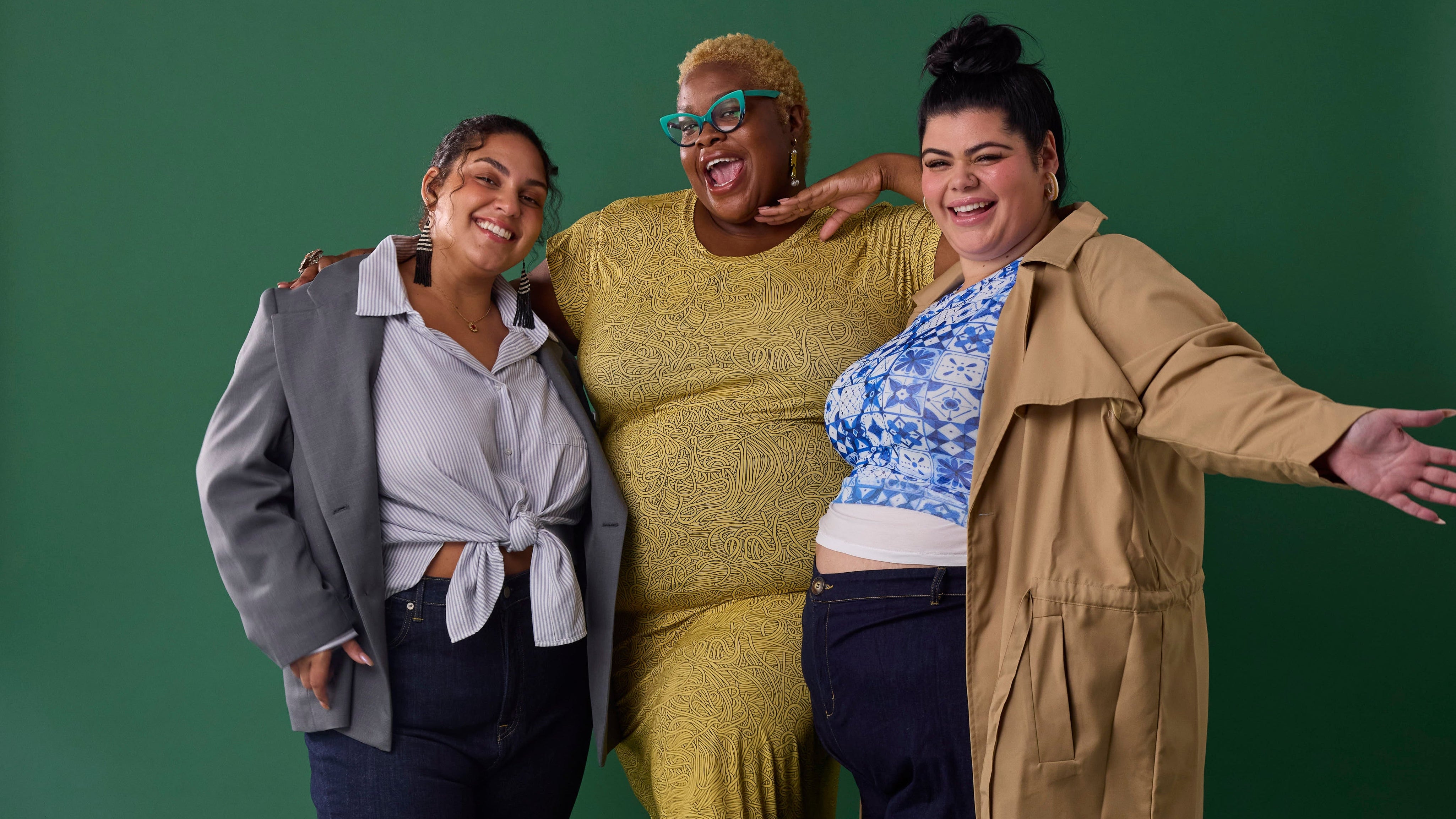 Three women posing together against a green background